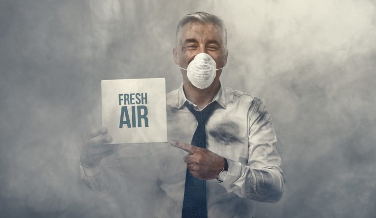 Confident man wearing a pollution mask and holding a fresh air sign