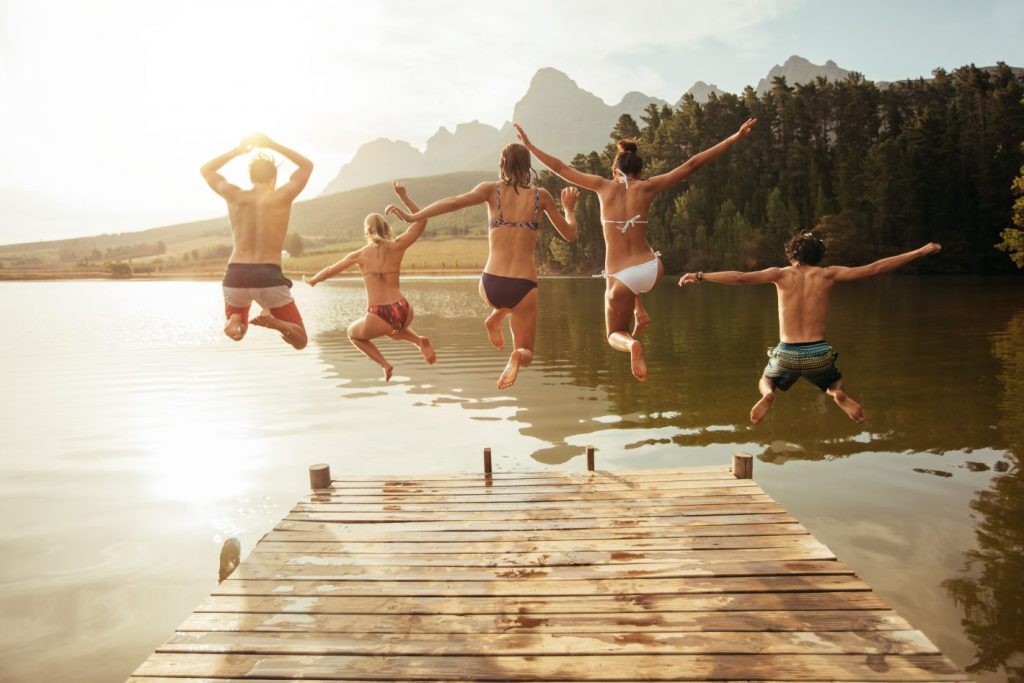 Portrait of young friends jumping from jetty into lake. Friends in mid air on a sunny day at the lake.