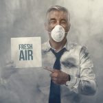 Confident man wearing a pollution mask and holding a fresh air sign