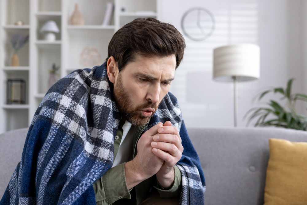 Man feeling cold and ill sitting on couch heater not working